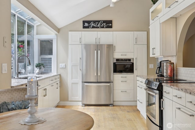kitchen featuring stainless steel appliances, a sink, vaulted ceiling, tasteful backsplash, and white cabinetry