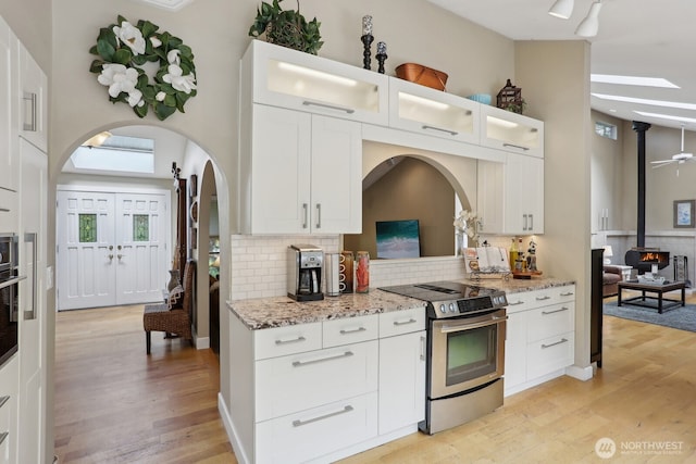 kitchen with stainless steel range with electric cooktop, a wood stove, arched walkways, light wood-type flooring, and backsplash