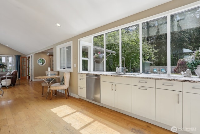 kitchen featuring a sink, stainless steel dishwasher, light wood-type flooring, vaulted ceiling, and light stone countertops