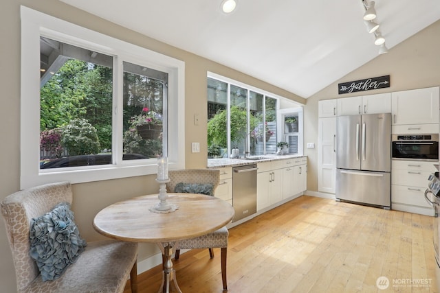 kitchen with stainless steel appliances, track lighting, light wood-style flooring, white cabinetry, and vaulted ceiling
