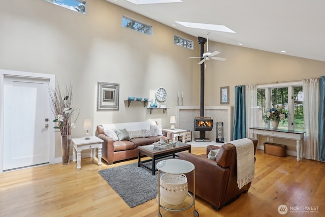 living area with high vaulted ceiling, a skylight, a wood stove, light wood-style floors, and recessed lighting