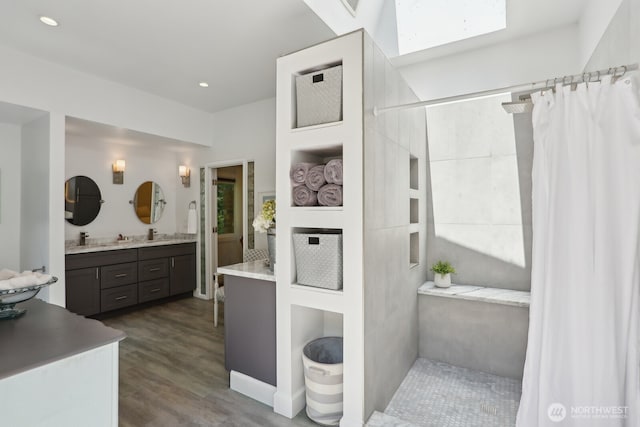 full bath featuring a skylight, a shower with curtain, wood finished floors, double vanity, and recessed lighting