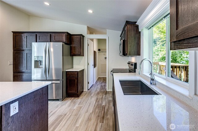 kitchen with dark brown cabinetry, stainless steel appliances, light stone counters, and a sink