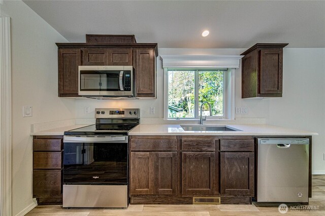 kitchen featuring a sink, visible vents, stainless steel appliances, light countertops, and dark brown cabinetry