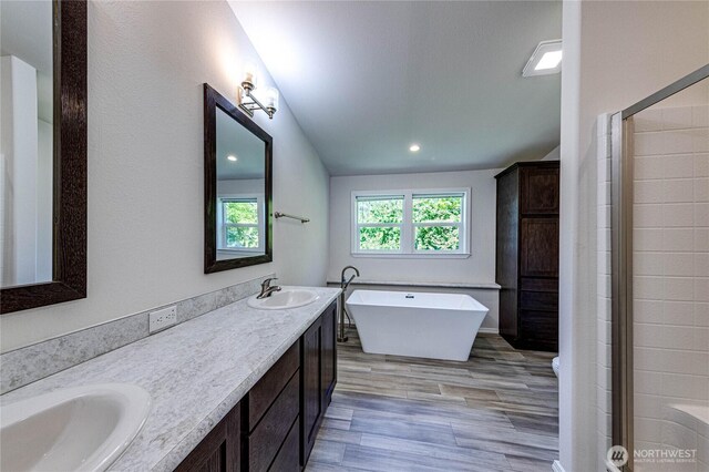 full bath with double vanity, a sink, a freestanding tub, and wood finished floors