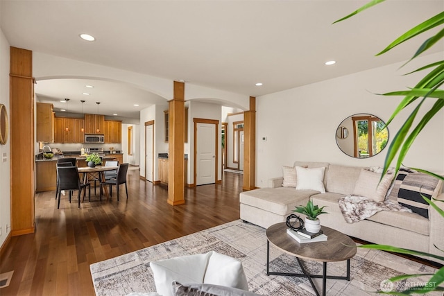 living area with dark wood-style flooring, arched walkways, recessed lighting, decorative columns, and visible vents