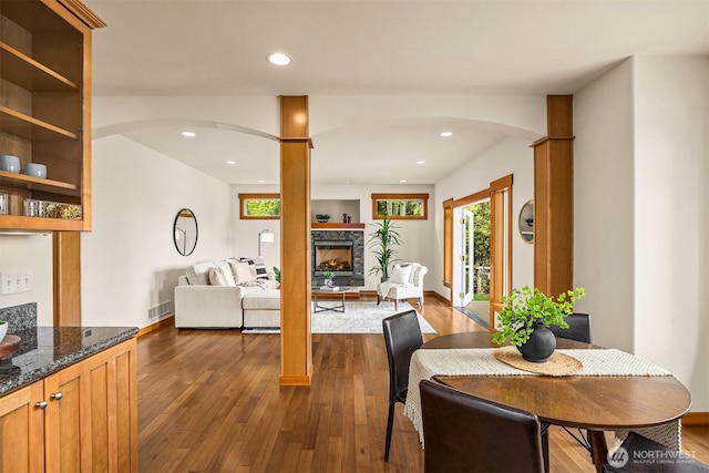 dining room featuring baseboards, dark wood-style floors, recessed lighting, a fireplace with raised hearth, and arched walkways
