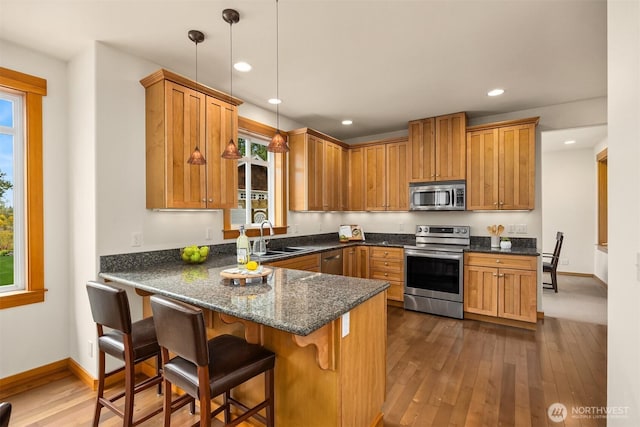 kitchen featuring dark wood-style flooring, appliances with stainless steel finishes, hanging light fixtures, a sink, and a peninsula