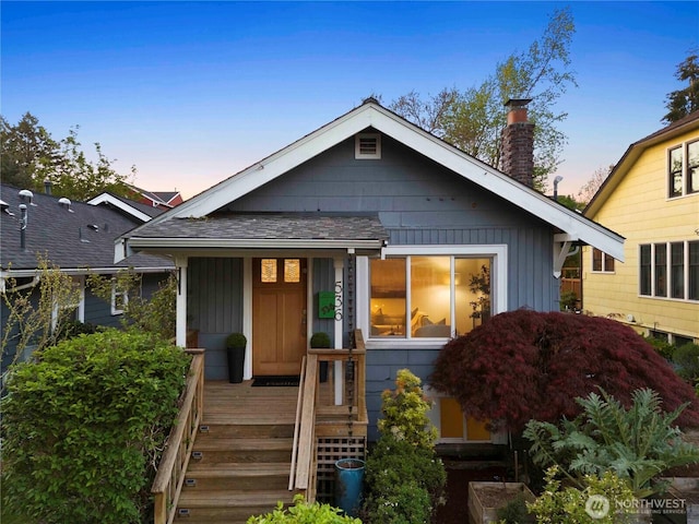 view of front of house with a porch, roof with shingles, and a chimney