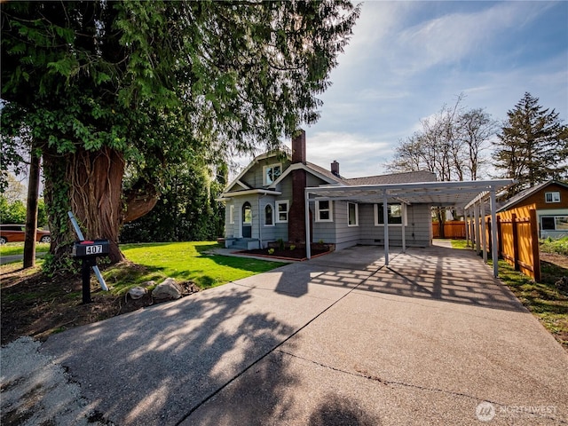 view of front of house with a front yard, driveway, a carport, a chimney, and fence