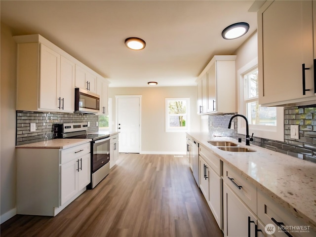 kitchen with light stone countertops, a sink, stainless steel appliances, tasteful backsplash, and baseboards