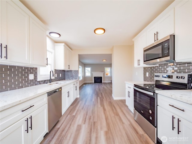 kitchen featuring light wood-style flooring, stainless steel appliances, a fireplace, a sink, and white cabinetry