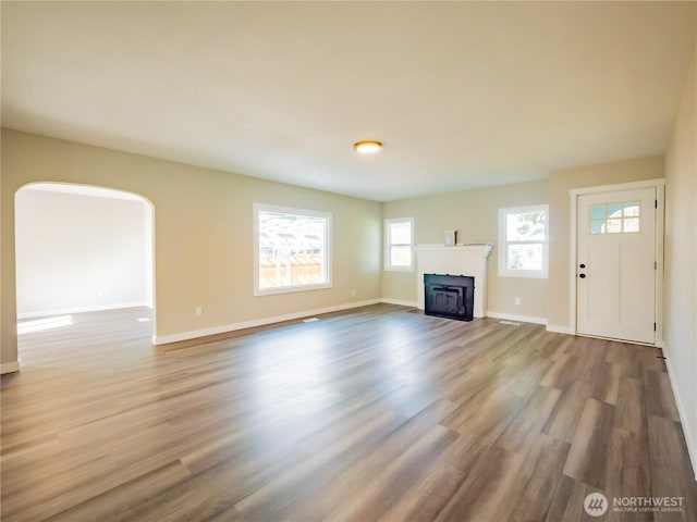 unfurnished living room with a fireplace with flush hearth, wood finished floors, and baseboards