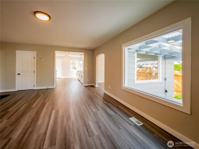 unfurnished living room with arched walkways, visible vents, baseboards, and dark wood-type flooring