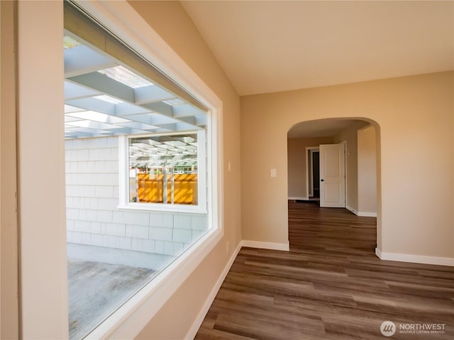 hall featuring dark wood-style floors, arched walkways, and baseboards
