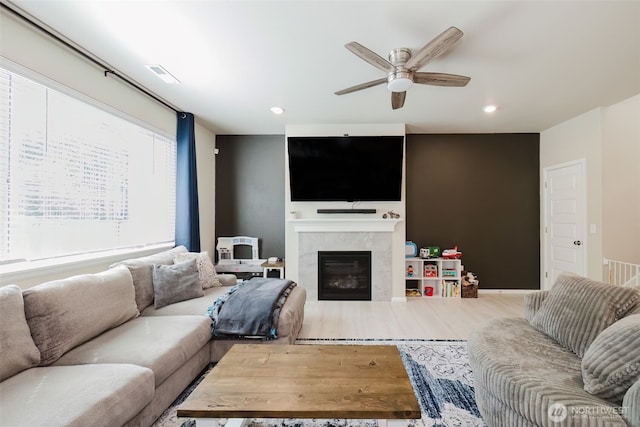 living room featuring ceiling fan, visible vents, a glass covered fireplace, and wood finished floors