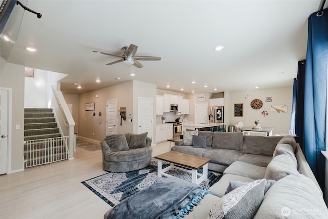 living area with a ceiling fan, light wood-type flooring, stairs, baseboards, and recessed lighting