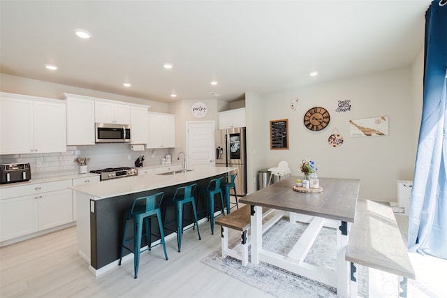 kitchen with white cabinets, a breakfast bar area, an island with sink, stainless steel appliances, and tasteful backsplash