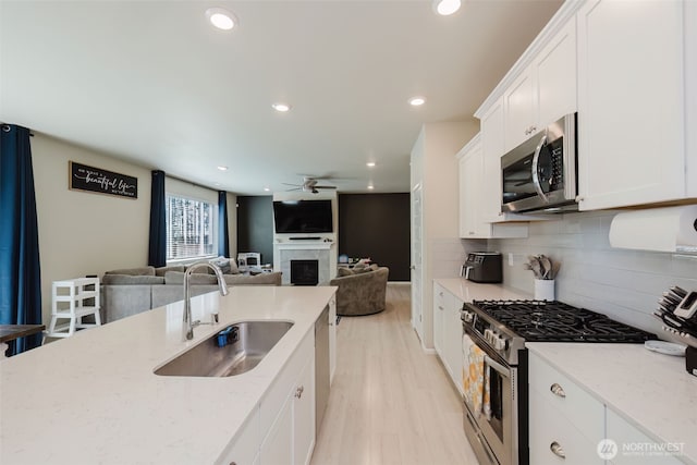 kitchen featuring ceiling fan, light stone countertops, a sink, stainless steel appliances, and backsplash