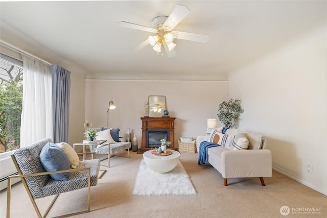 sitting room with a glass covered fireplace, baseboards, ceiling fan, and light carpet