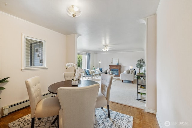 dining area with a glass covered fireplace, baseboard heating, and ceiling fan