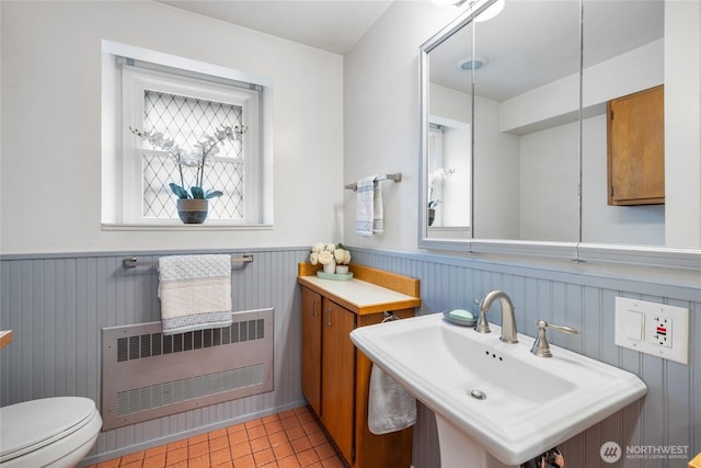 half bathroom featuring radiator heating unit, a wainscoted wall, a sink, and a wealth of natural light