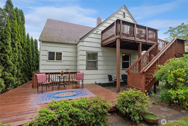 back of house with roof with shingles, outdoor dining space, a chimney, and a deck