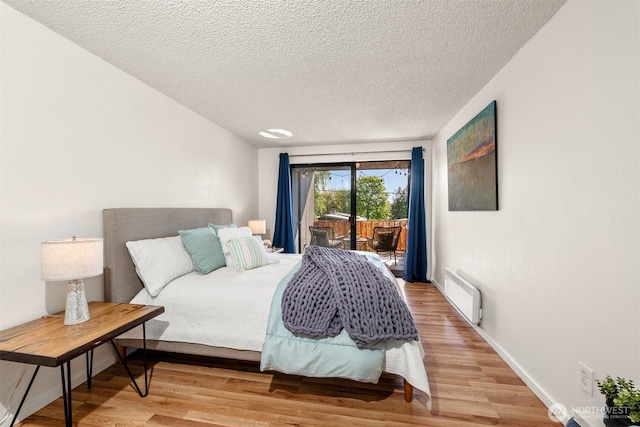 bedroom featuring light wood-style floors, a textured ceiling, access to exterior, radiator heating unit, and baseboards