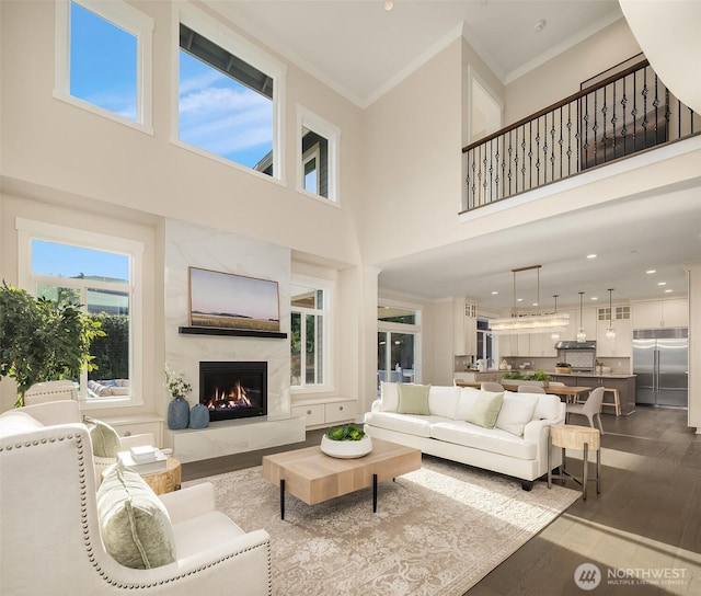 living area with a high end fireplace, crown molding, dark wood finished floors, a towering ceiling, and recessed lighting