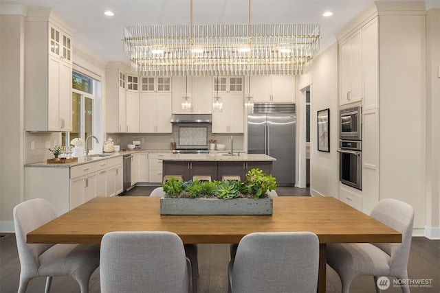 kitchen featuring built in appliances, under cabinet range hood, a center island with sink, a sink, and decorative backsplash
