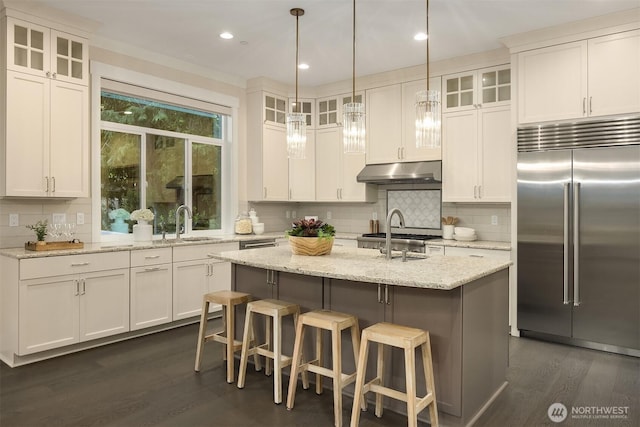 kitchen featuring built in fridge, under cabinet range hood, dark wood-style floors, decorative backsplash, and a sink