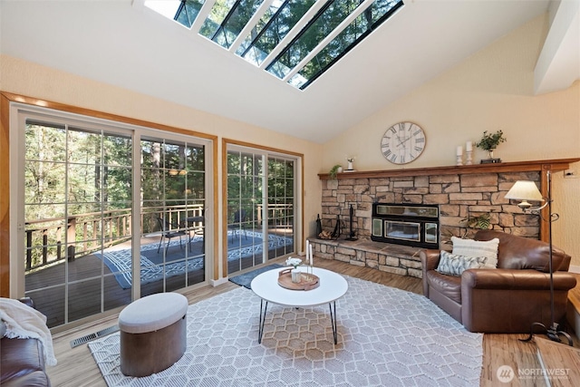 living room with wood finished floors, high vaulted ceiling, and a stone fireplace