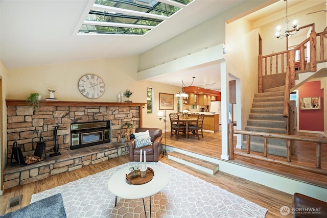 living area with wood finished floors, an inviting chandelier, a stone fireplace, visible vents, and high vaulted ceiling
