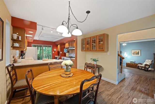 dining room featuring rail lighting, light wood-style flooring, stairs, and baseboards