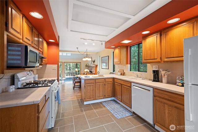 kitchen featuring a sink, tile counters, a peninsula, and white appliances