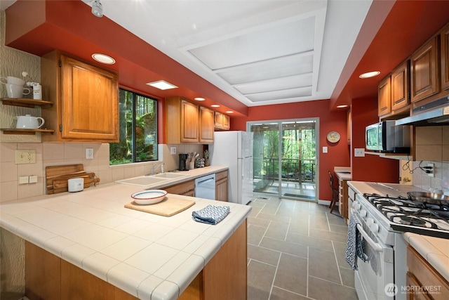 kitchen featuring stainless steel appliances, tile countertops, under cabinet range hood, and a sink