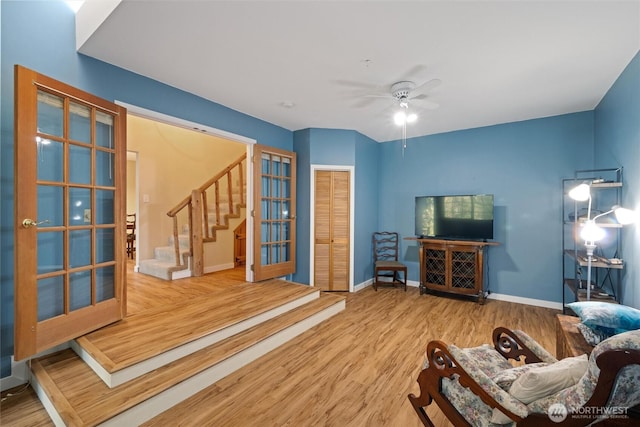 living room featuring stairway, ceiling fan, french doors, baseboards, and wood finished floors