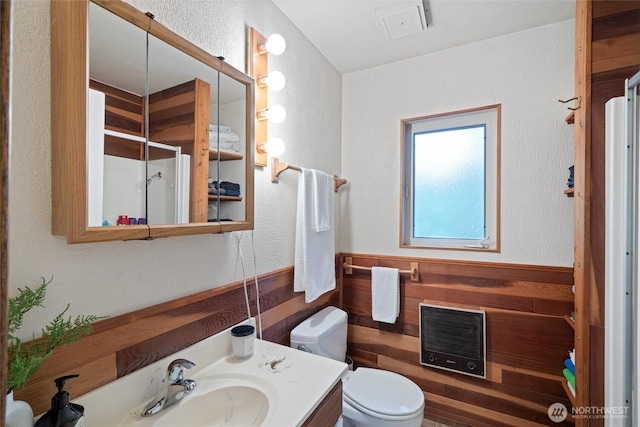 bathroom featuring a shower stall, vanity, heating unit, toilet, and wooden walls