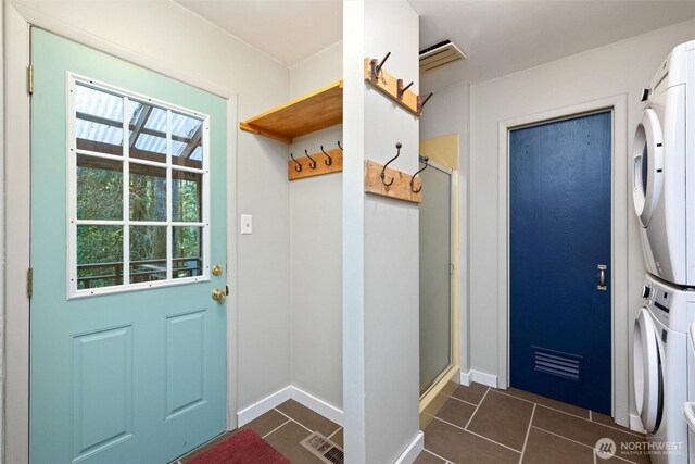 mudroom featuring stacked washer / drying machine, visible vents, baseboards, and dark tile patterned flooring