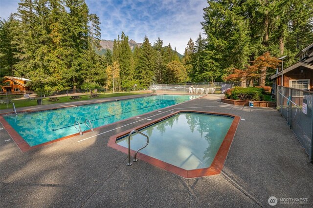 pool featuring fence, a patio area, and a forest view