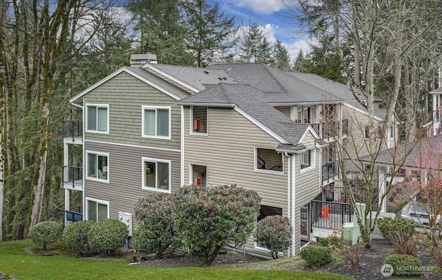 rear view of property with a chimney, a balcony, and roof with shingles