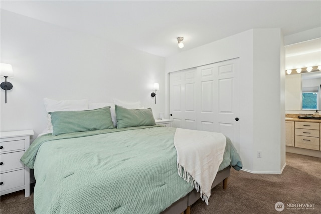 bedroom with a closet, baseboards, ensuite bathroom, and dark colored carpet