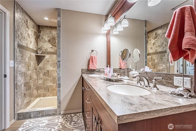 bathroom with double vanity, walk in shower, baseboards, and a sink