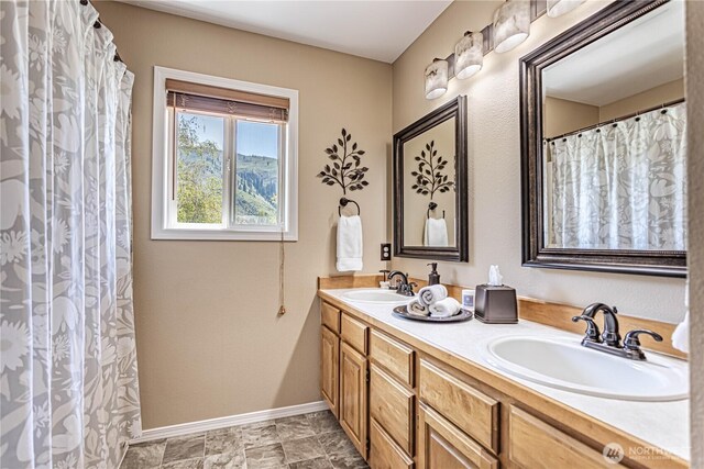 full bath with baseboards, double vanity, and a sink