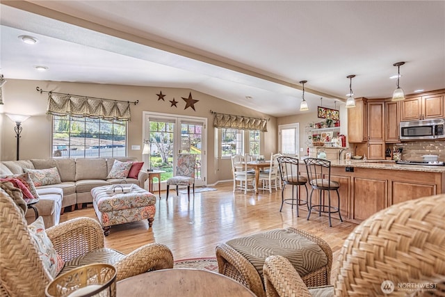 living room featuring lofted ceiling, light wood finished floors, and baseboards