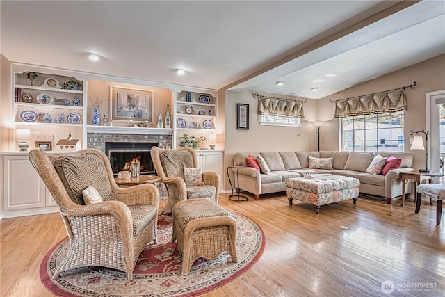 living room with a brick fireplace, vaulted ceiling, built in features, and light wood-style floors