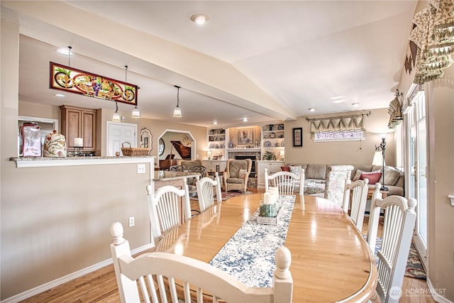 dining area with baseboards, light wood-type flooring, a fireplace, and vaulted ceiling