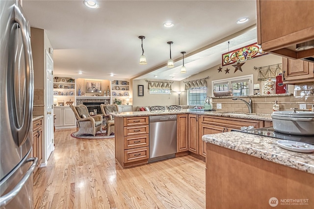 kitchen featuring a tile fireplace, light wood-style flooring, light stone counters, appliances with stainless steel finishes, and a sink