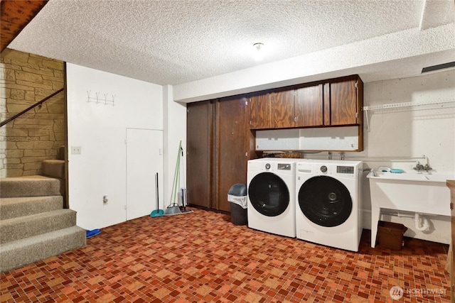 washroom featuring a sink, washing machine and dryer, a textured ceiling, and cabinet space