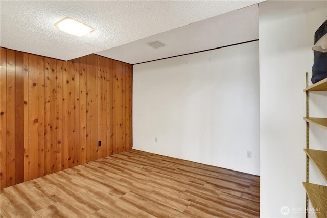 spare room featuring a textured ceiling, wood walls, and wood finished floors